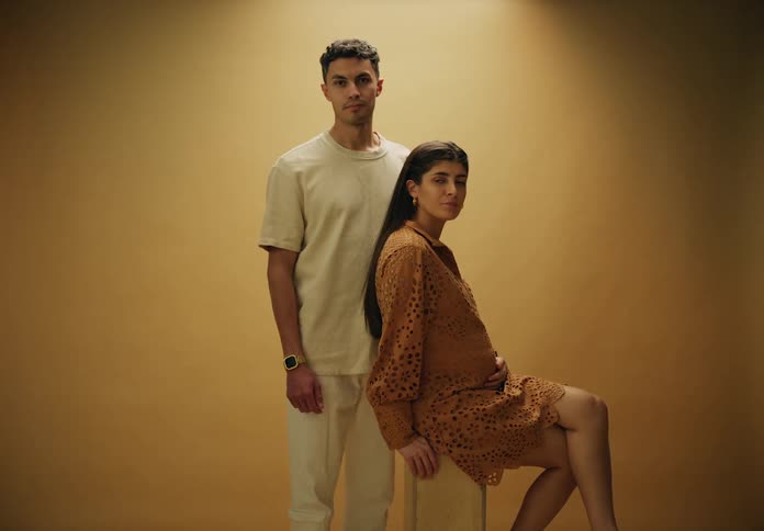 Man standing next to pregnant wife sitting both posing