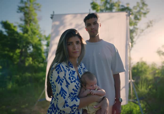 Mother with a baby on her lap and the father in the background while they are on a hill with a white screen in the background