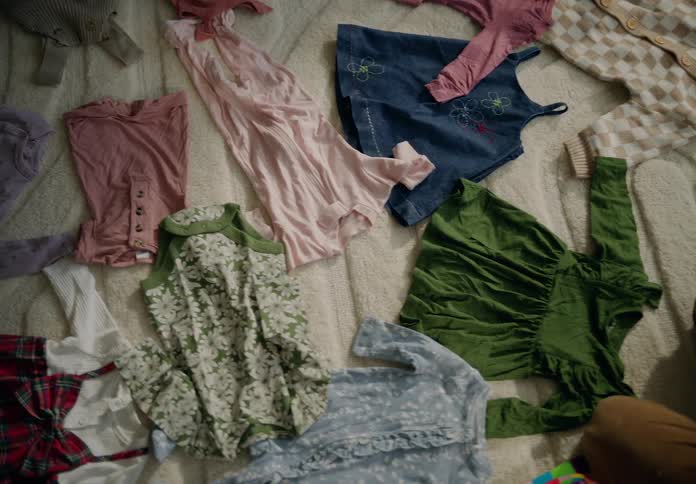 Person in the middle of baby clothes on a rug