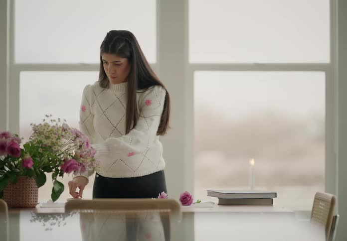 Woman at a table picking up pink flowers next to it