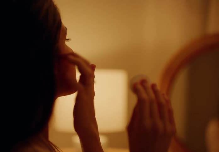Woman sitting in front of a round mirror putting on makeup