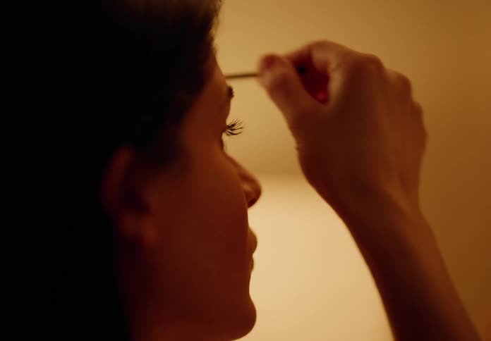 Closeup of a woman applying makeup in a dimly lit room