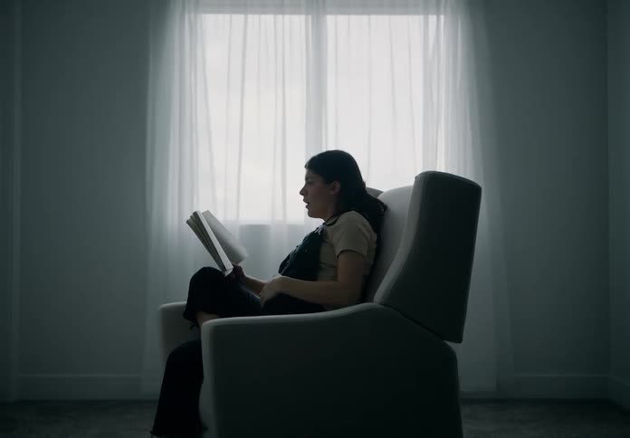 Pregnant woman sitting in an armchair reading a book and a man handing her a blanket