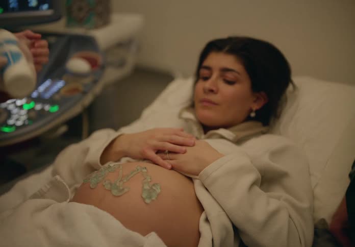 A pregnant woman is lying on a bed and someone is applying cream to her belly to do an ultrasound