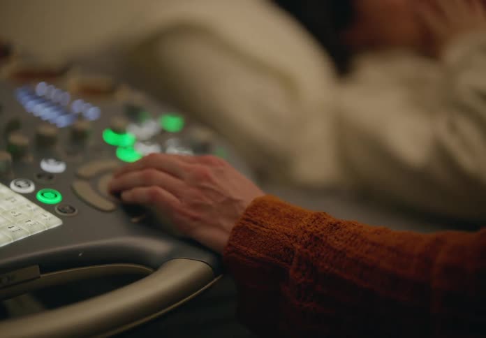 A hand operating a sonogram machine while a woman is lying next to it