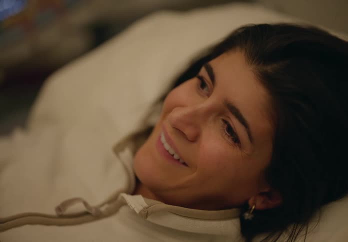 A dark haired woman smiles while lying in a bed