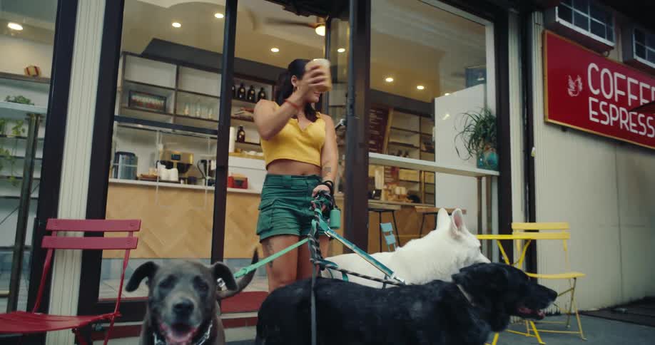 A woman walks out of a coffee shop with a cup on her hand ready to walk several dogs