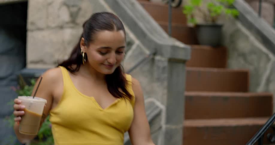 A young woman is walking down some stairs with some dogs and then she stops to drink a liquid from a brown cup