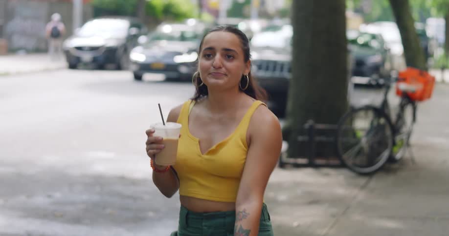 A young woman is walking several dogs on a neighborhood sidewalk while drinking iced coffee