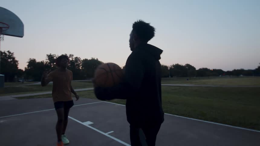A couple of friends are greeting each other on a basketball court at sunset