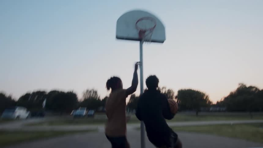 A couple of friends are engaged in a competitive game of basketball on a court at sunset