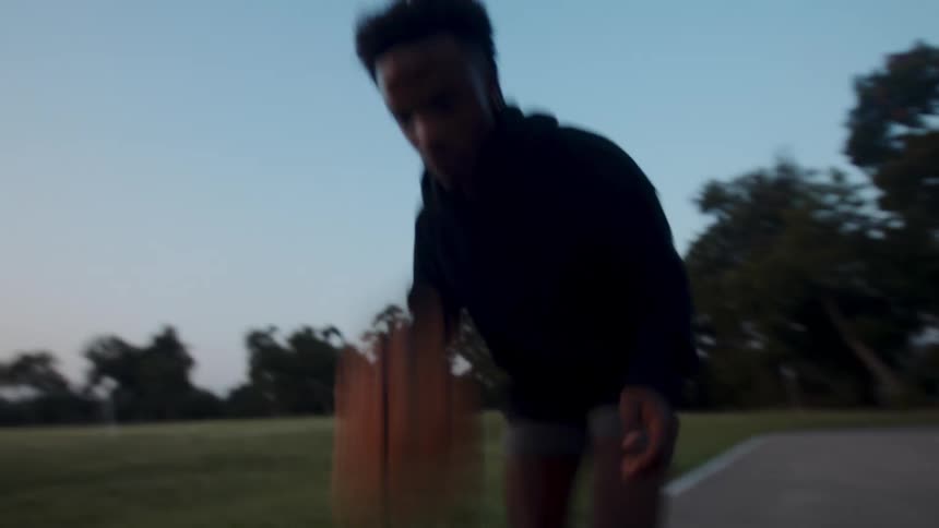 A man is dribbling a basketball on a court in the park during the evening