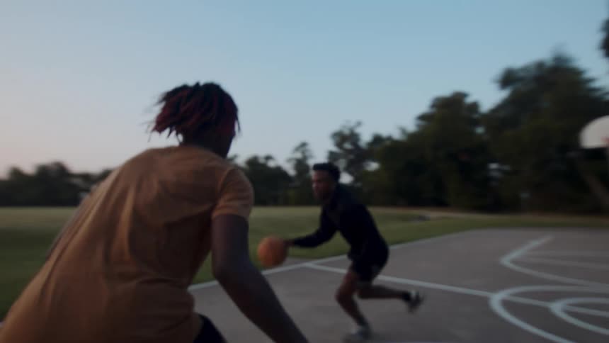 Two boys playing basketball on a court in the late afternoon