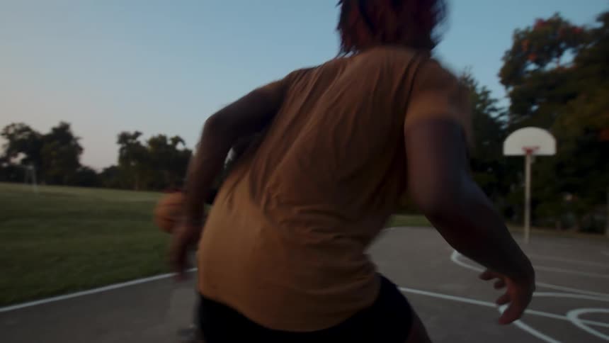 A couple of friends are engaged in a competitive game of basketball on a court at sunset