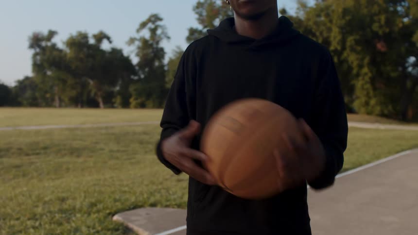 Young man tossing a basketball from one hand to the other on the side of a court