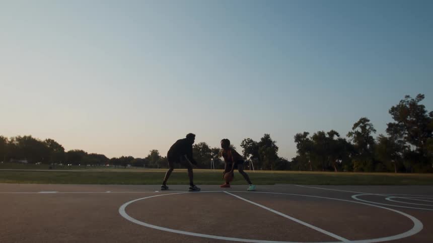 Two people playing basketball on an outdoor court and one of them shoots the ball