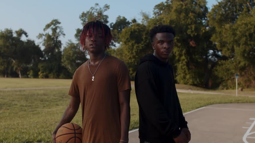 Two young men standing side by side with one of them holding a basketball