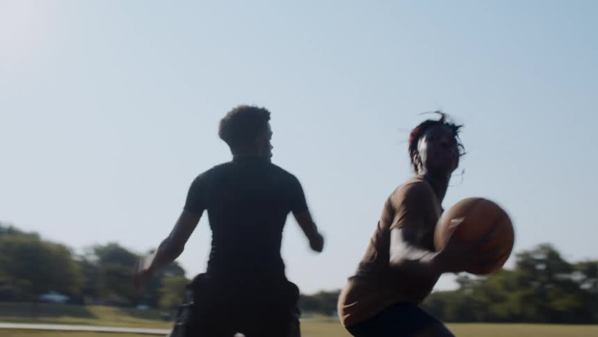 A couple of friends are engaged in a competitive game of basketball on a court at sunset