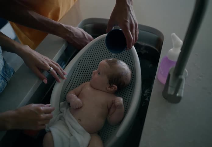 Parents bathe their baby in the kitchen sink