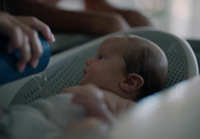 A woman is happy while bathing a newborn baby using a blue cup