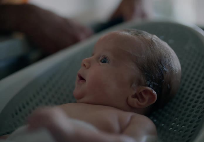 An adult hand bathing the head of a newborn baby who is shirtless