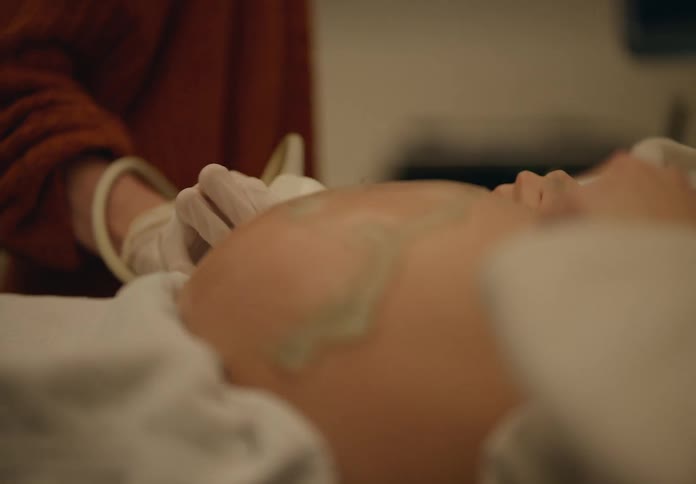 Nurse with equipment rubbing a pregnant womans belly with a gel