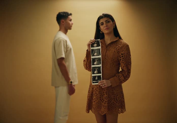 Man standing in the background and in front a pregnant woman holding an ultrasound in a studio