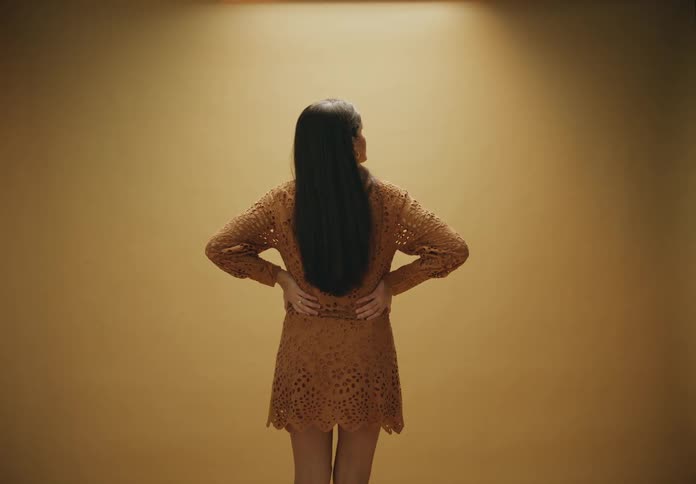 A pregnant woman standing against a beige background wearing a dress