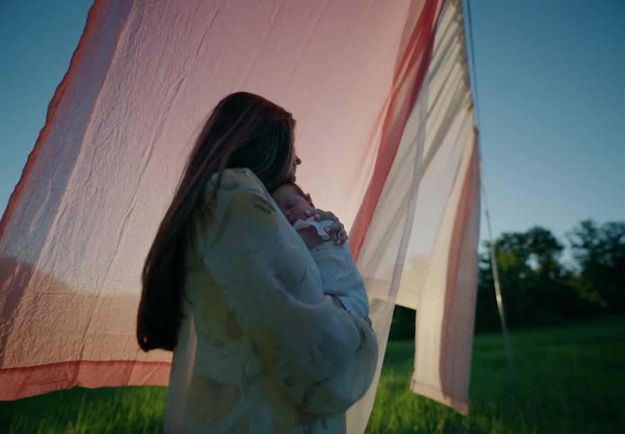 Mother holding her baby in her lap with a scarf on a clothesline next to her in a natural setting
