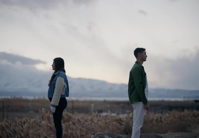 Man and a pregnant woman standing back to back in a landscape with mountains in the background