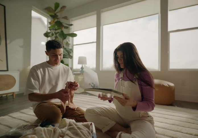 Pregnant woman looking at a book next to a man looking at baby clothes