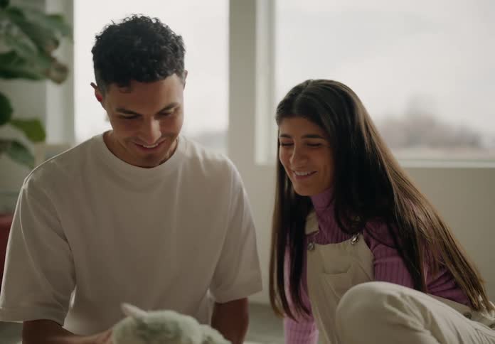 Husband and wife smile over a stuffed toy while sitting on their living room floor