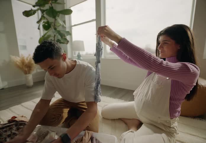 Happy man and woman sitting in living room looking at box of baby clothes