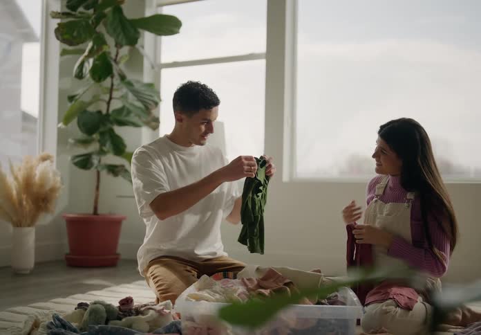 Expectant parents sort baby clothes while smiling and conversing with each other