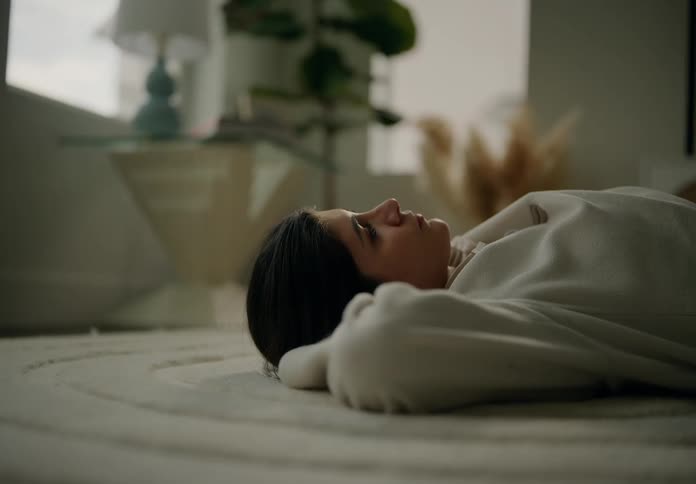 A woman lying on the living room floor looking at the ceiling