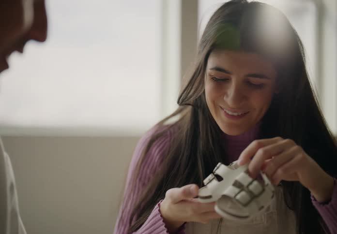 Couple sitting in living room looking at newborn clothes and sneakers while the woman is pregnant and both kiss romantically