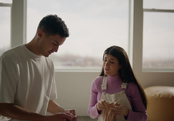 Couple with a pregnant woman sitting on the living room rug looking at baby clothes together
