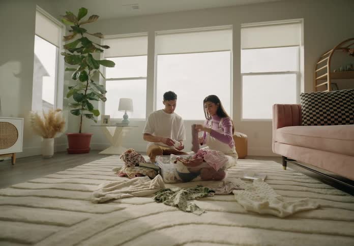 Man and woman sitting in living room looking at newborn baby clothes