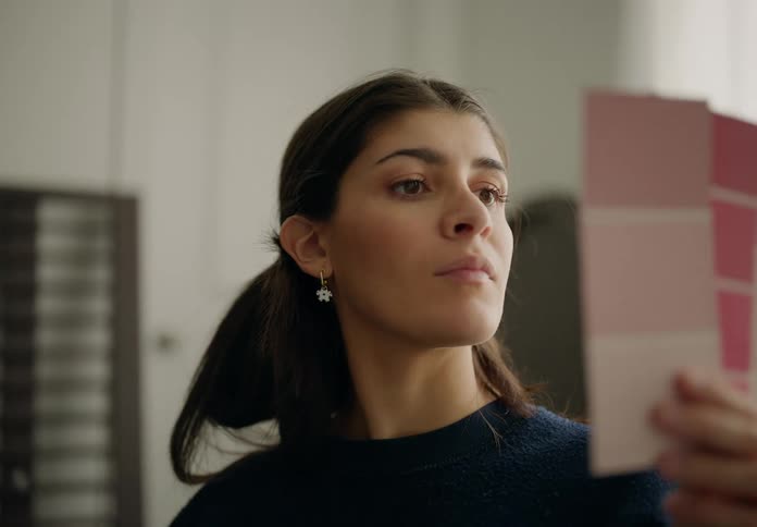 The face of a young woman with her hair tied back and was looking at three papers with pink colors and looking up