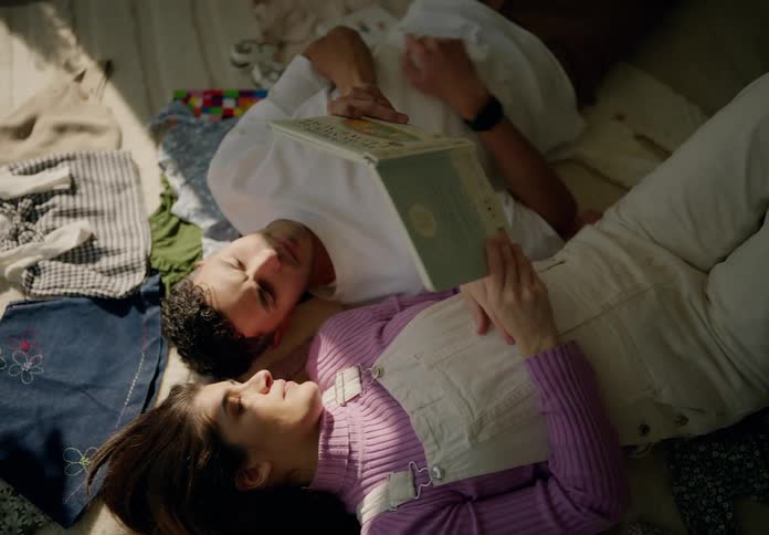 A man and woman read a book while laying on the carpet