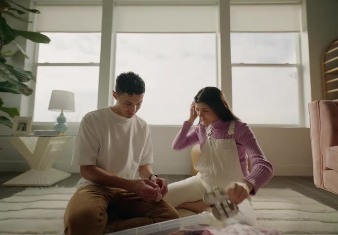 A man and a woman are happy and see each other kissing while they are sitting and looking at baby clothes that are in a large plastic bag on the floor