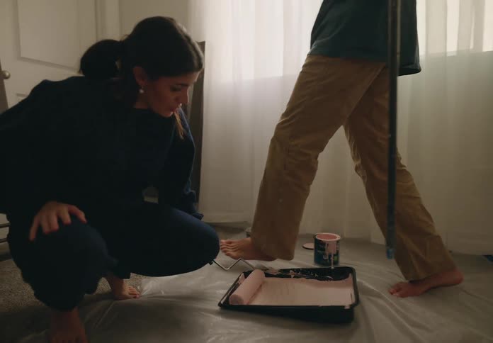 A man and a woman using roller brushes to paint a bedroom