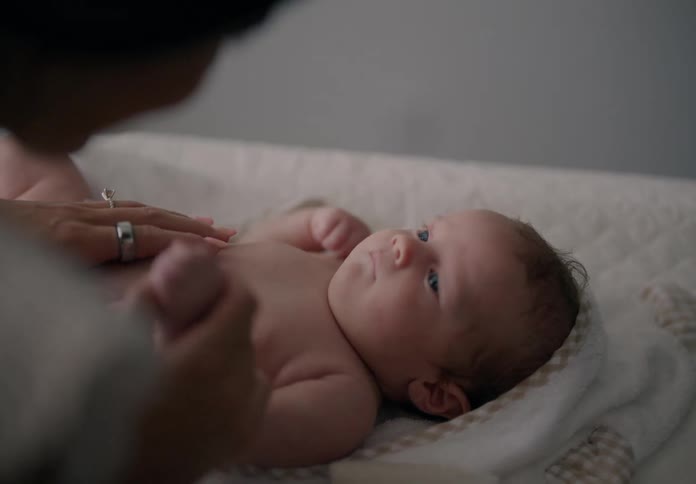 Closeup of a newborn baby resting in a bed with a woman holding the babys hand