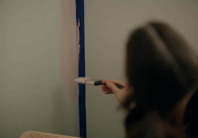 A woman applies pink paint with a brush on a wall at home
