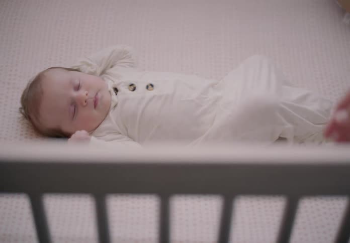 A parents hands leaves a sleeping baby on a white crib