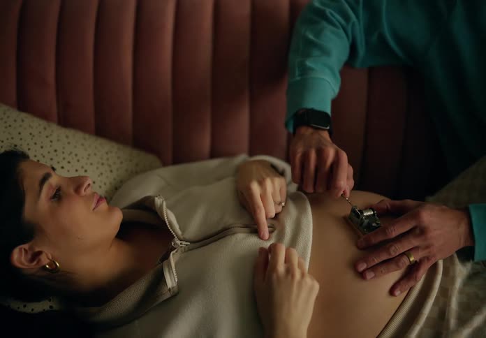 A hand playing a music box on a pregnant womans belly