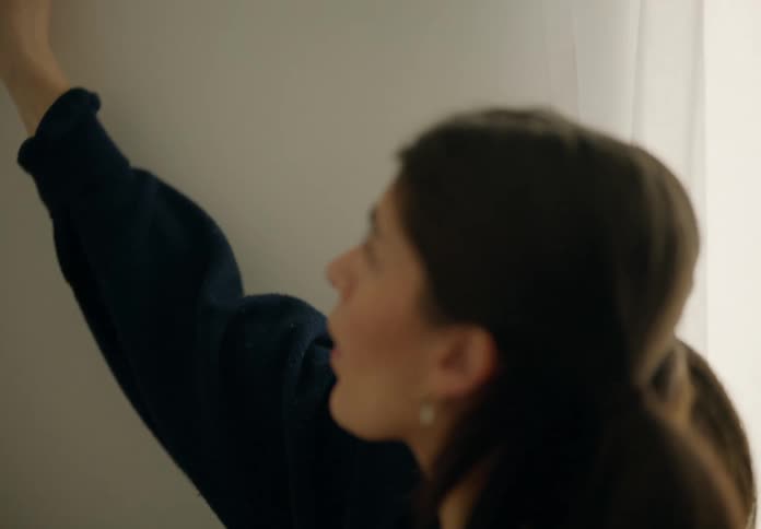 Woman wears a sweatshirt while using a paintbrush to paint an interior wall