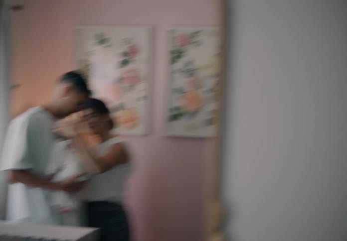 Man with a baby in his arms next to the woman in a loving moment seen in the reflection of a mirror