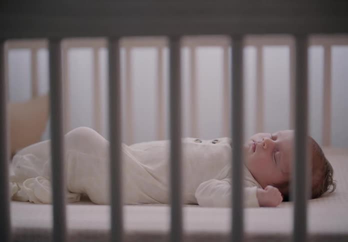A little baby in white clothes is sleeping in a crib