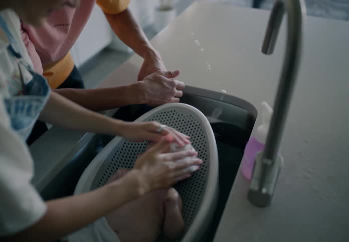 Father and mother together bathing newborn baby in kitchen sink